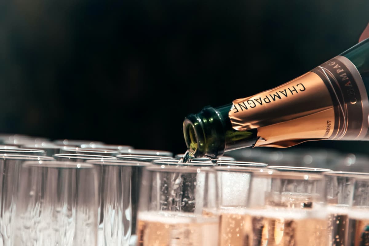 Champagne being poured out of a bottle with many glasses lined up.