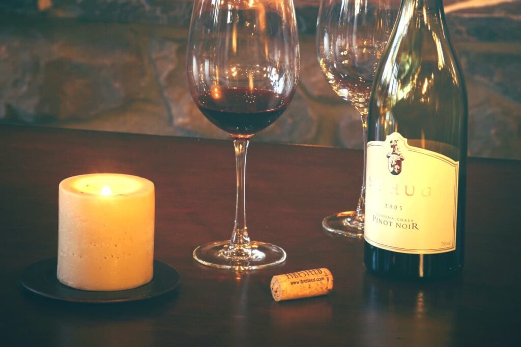 A bottle of pinot noir and glasses on a wooden table.